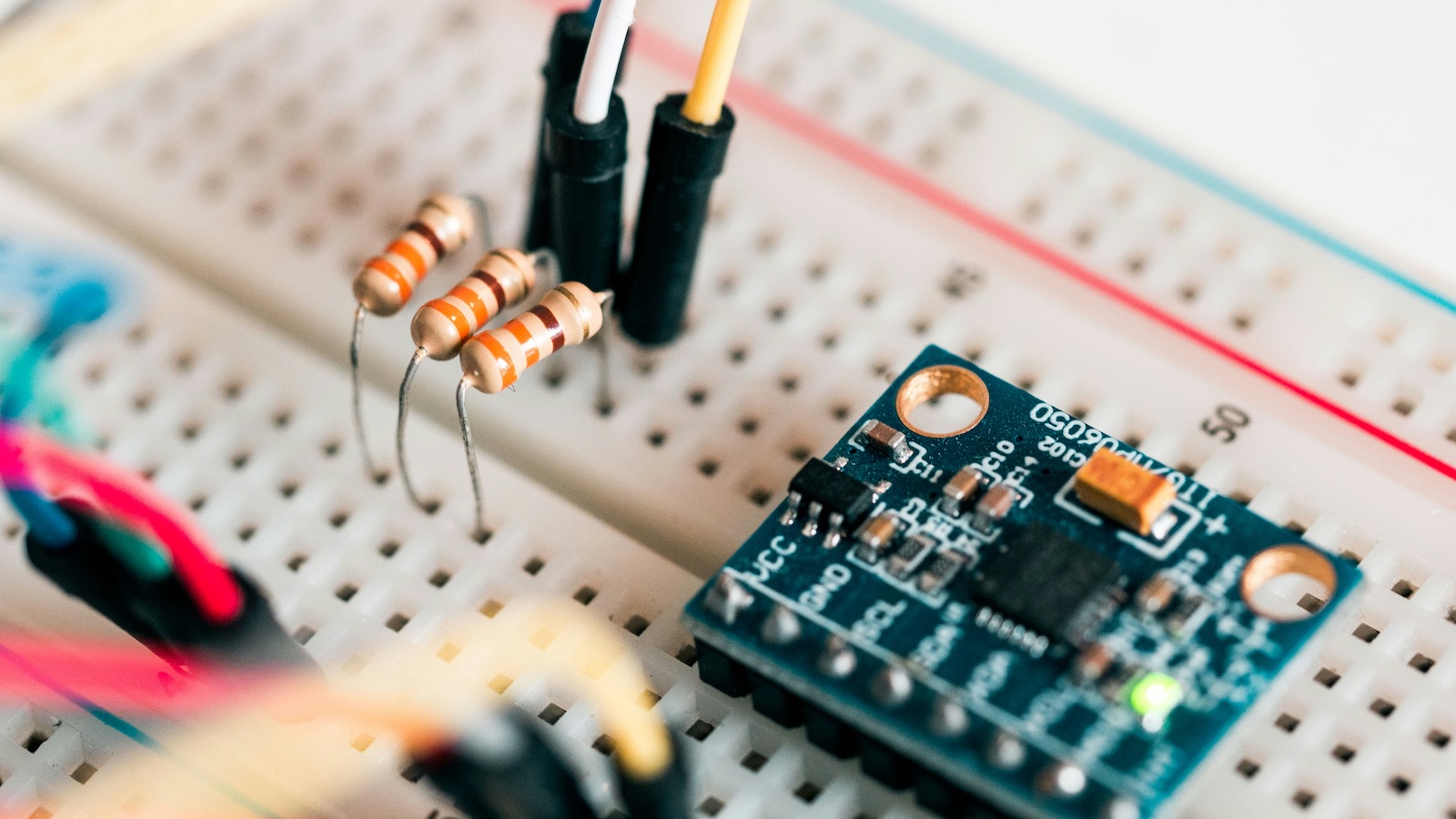 Beginner electronics lesson showing a simple LED circuit built on a breadboard with jumper wires.